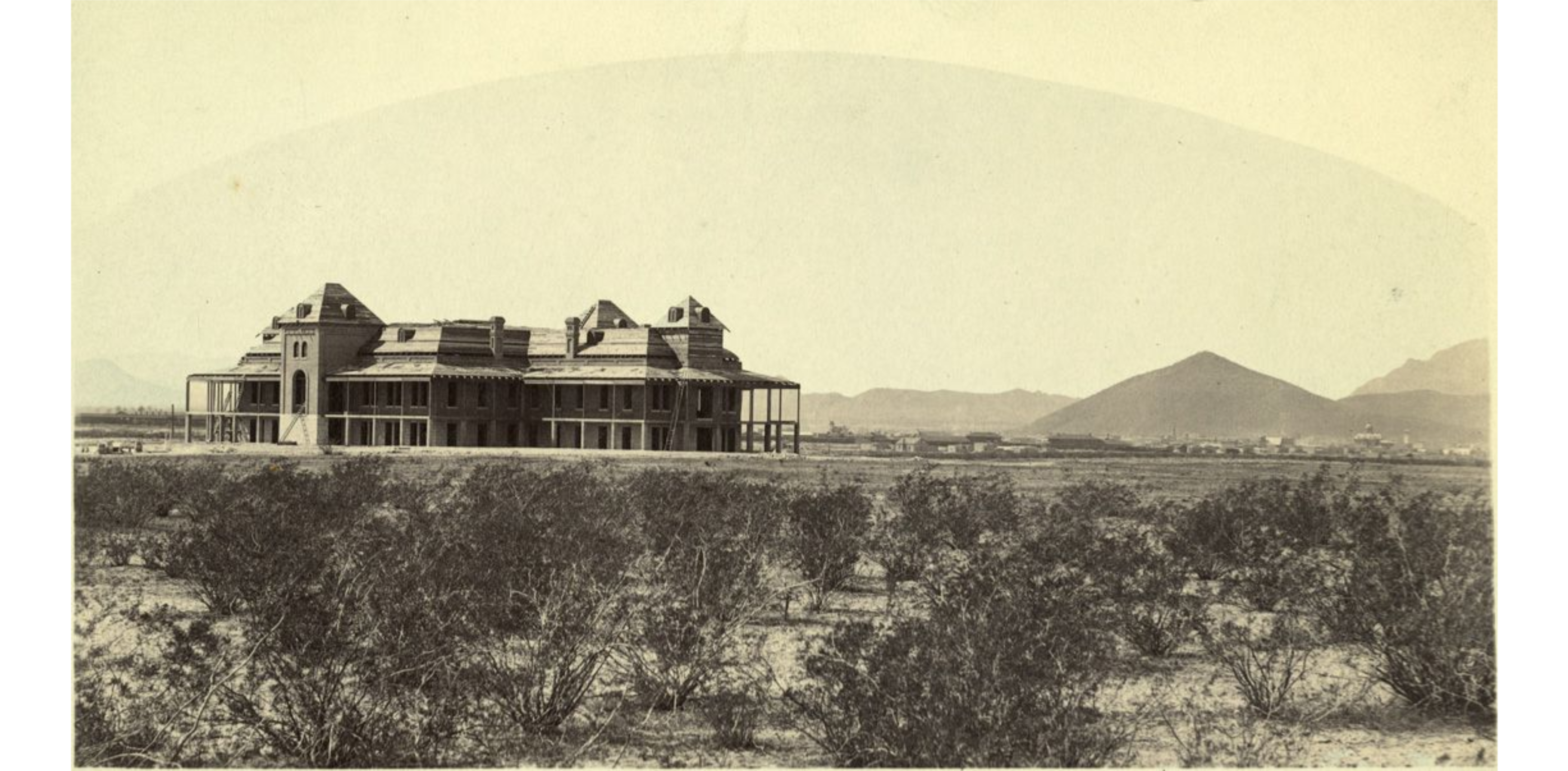 The 1st building at the University of Arizona (Old Main) being constructed in the middle of the desert. The city of Tucson is in the background. The photo is Looking west.
